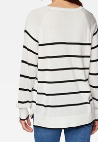 Maglione leggero a maniche lunghe di colore bianco con strisce orizzontali nere. Presenta una vestibilità rilassata e un bordo arrotondato con fessure laterali.