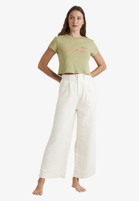 Grön crop top med blommönster broderat på framsidan, i kombination med lösa, vita, texturerade vida byxor med hög midja och två knappar.