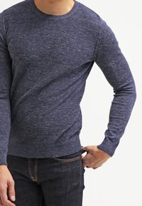 Pull tricoté bleu marine avec un col rond, des poignets et une ceinture côtelés ; présente un motif texturé et une coupe décontractée.