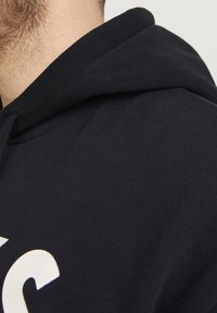 Schwarzer Hoodie aus weich verarbeitetem Stoff, mit einem kontrastierenden weißen Logodetail und einem klassischen Kordelzugdesign.