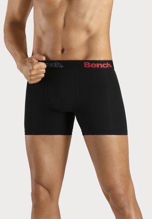 Schwarze Boxershorts mit enger Passform und einem Logo-Bund in Rot und Grau. Glatte Textur und mittellange Beine.