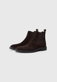Botas Chelsea de ante marrón oscuro con paneles laterales elásticos, puntera redondeada y suela de goma. Incluyen una lengüeta en la parte trasera para facilitar su colocación.