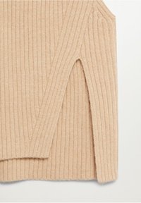 Manche de pull en tricot côtelé beige avec épaule visible et fente latérale sur un fond clair.