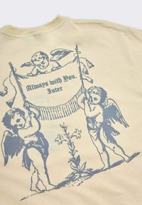 T-shirt beige chiaro con una grafica blu di cherubini che tengono un banner con il testo "Sempre con Te. Juter" e accenti floreali sotto.