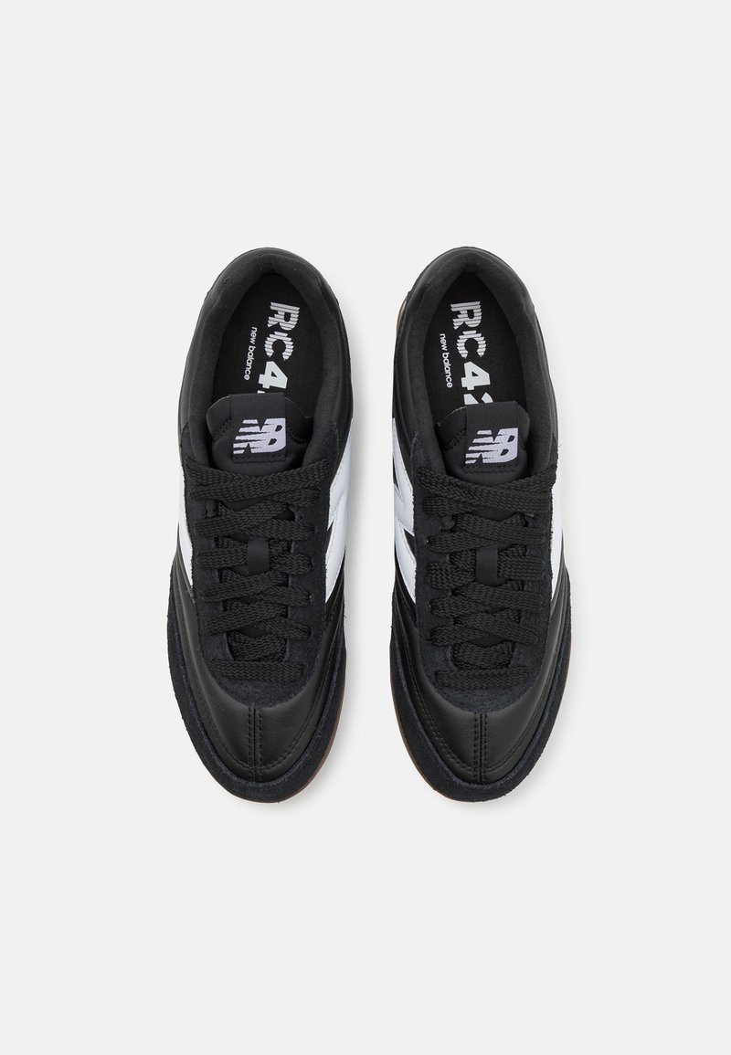 Scarpe da ginnastica nere con un design a collo basso, caratterizzate da strisce bianche ai lati, lacci neri testurizzati e una suola in gomma.