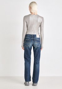Camiseta de manga larga metálica gris combinada con vaqueros de denim azules con un ligero desgastado y un parche de marca en la parte posterior. Diseño simple de pierna recta.