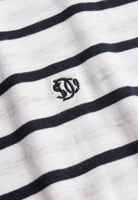 Hvidt stof med jævnt fordelte vandrette sorte striber og et lille sort broderet monogram i vintage-stil i midten.