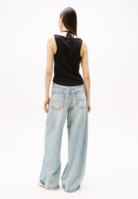 Black sleeveless top with a tie closure at the back, paired with light blue wide-leg jeans featuring back pockets. Smooth texture.