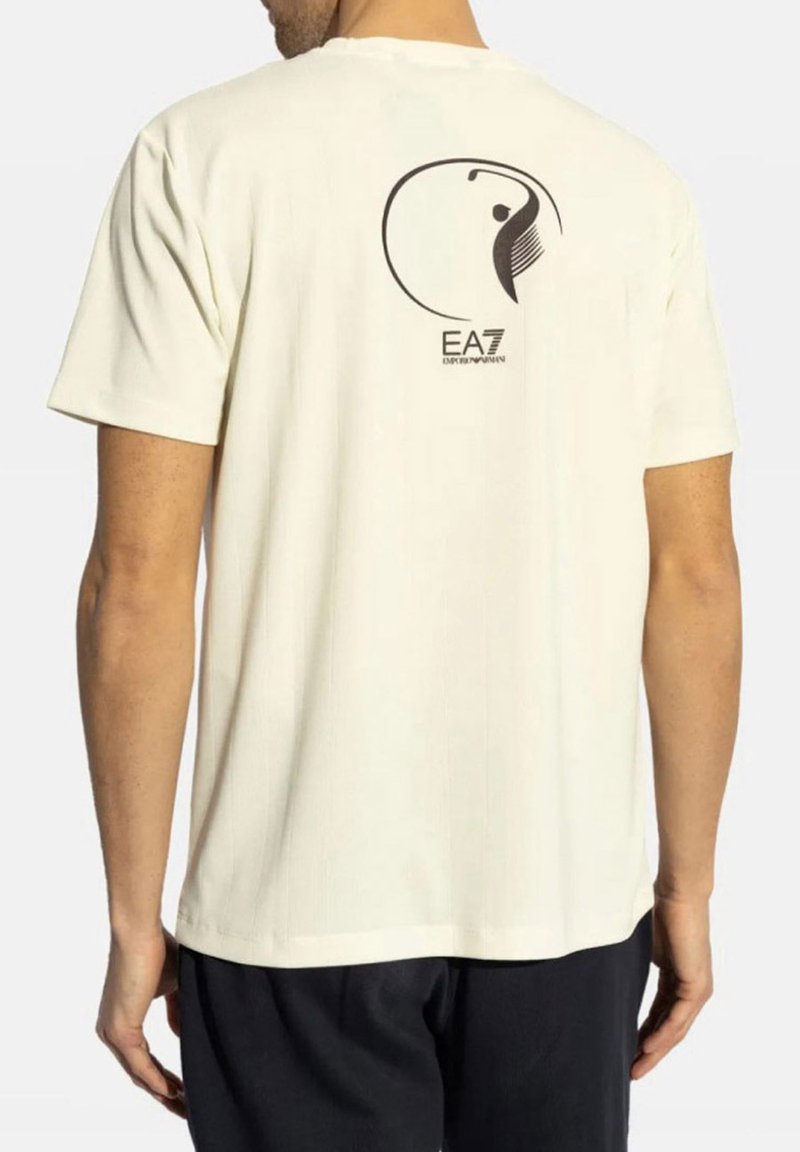 T-shirt color crema realizzato in tessuto morbido con scollatura rotonda. Presenta un logo grafico nero e un design sul retro. Maniche corte.