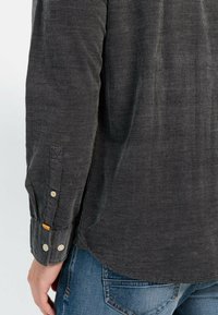 Long-sleeve shirt in dark gray fabric with a textured pattern. Features buttoned cuff and side slit hem, paired with blue denim jeans.