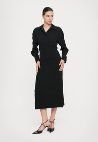 Rochie neagră cu mânecă lungă, guler, corset ajustat și fustă dreaptă. Purtați cu tocuri negre cu vârf ascuțit și curea la gleznă.