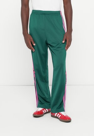 Green athletic pants with pink side stripes. Made of a lightweight material, featuring an elastic waistband and a relaxed fit.