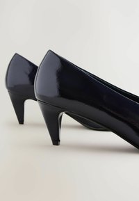 Musta lakattu nahkakengät korkeohrilla, joissa on kiiltävä pinta, terävä nenä ja kapeneva stiletto-korko.