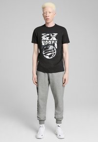 Sort t-shirt med grafisk print, grå sweatpants og hvide sneakers. T-shirten har en rund hals; sweatpantsene er elastiske ved anklerne.
