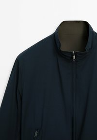 Navy zip-up jacket with a high collar, featuring a smooth, lightweight fabric and a side zip pocket. Interior has a contrasting color.