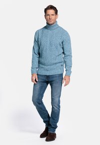Lichtblauwe coltrui met een textuur van kabelsteek, gecombineerd met donkerblauwe jeans en bruine suède laarzen. Een eenvoudige en casual look.