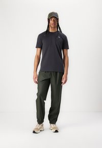 Dunkelgraues T-Shirt mit kurzen Ärmeln, grüne Hose mit elastischen Bündchen, beiges Sneaker mit schwarzer Sohle und eine Camouflage-Mütze. Schlichtes Design und lässige Passform.