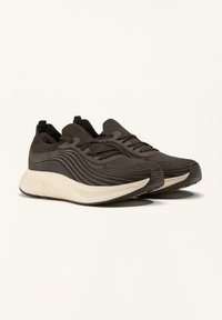 Zwarte sportschoenen met een textuur van gebreid bovenwerk, met golvende patronen, platte veters en een witte, gevoerde zool.