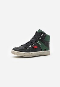Zapatilla alta con cuero negro y paneles de malla verde. Presenta una suela de goma gris, ojales de metal y una etiqueta de logo roja en el lateral.