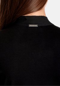 Top in maglia nera con collo alto, caratterizzato da una sottile texture e un'etichetta in metallo sul retro, incentrato su un design minimalista.
