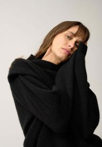 Przesadny czarny sweter robiony na drutach z wysokim, prążkowanym kołnierzem i długimi, owiniętymi rękawami, prezentujący miękką teksturę i minimalistyczny design.