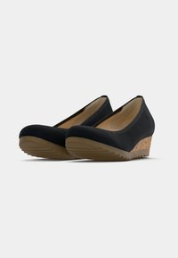 Chaussures noires à talon compensé bas, semelles intermédiaires en liège et semelles en caoutchouc, positionnées en angle côte à côte sur un fond blanc.