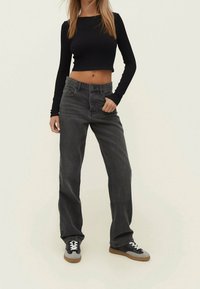 Top crop de manga larga negro combinado con jeans de mezclilla gris de tiro alto y zapatillas gris y negro, con cordones blancos y suela plana.