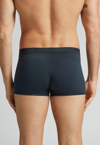 Mörkblå boxerkalsonger med en mjuk, slät textur, utrustade med ett märkes-elastiskt midjeband och en åtsittande design, visade från baksidan.