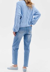 Ljusblå stickad tröja med ett strukturerat diamantmönster, kombinerad med ljusblå jeans och pastellblå sneakers.