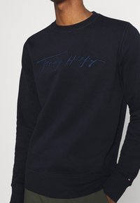 Navyblauwe sweatshirt met een ronde hals en lange mouwen. Kenmerkt zich door het geborduurde "Tommy Hilfiger" logo in bijpassende draad. Katoenmengsel.
