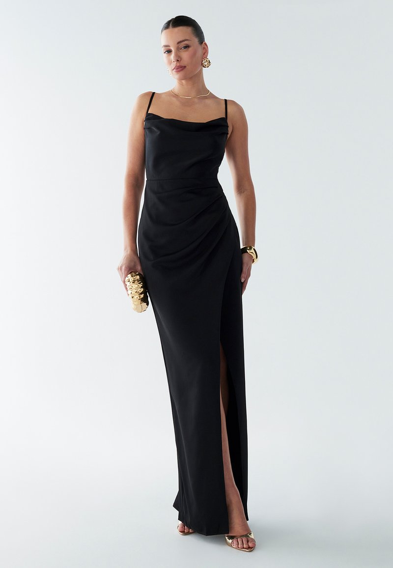 Black satin evening gown with a cowl neckline, draped detail, and high side slit. Paired with a gold clutch and metallic sandals.