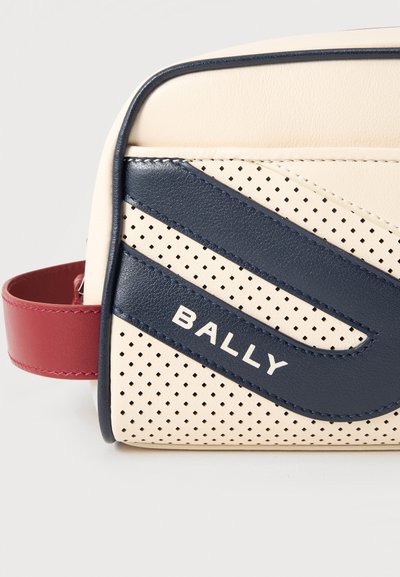 Trousse rectangulaire en cuir crème avec motif perforé, rayures diagonales bleu marine, sangle latérale rouge et logo "BALLY" sur le devant.