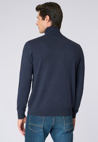 Maglione pullover blu navy con colletto alto, polsini e orlo a costine, realizzato in un morbido tessuto testurizzato. Indossato con jeans blu.