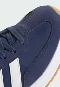 Marinblå sneakers i mocka och textil. Har vita ränder, strukturerad yta och en gummisula. Sömmarna är synliga längs kanterna.