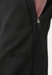 Črne atletske kratke hlače z mrežasto ploščo, žepom na zadrgo in embosiranim logotipom "BOSS". Narejene iz strukturirane, zračne tkanine.