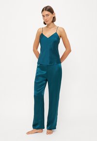 Teal satin sovensett som inkluderer en cami med tynne stropper og vide bukser. Glatt tekstur, avslappet passform og minimalt design.