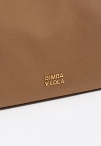 Bolsa de tela marrón con una textura suave, que presenta el logotipo dorado en relieve "BIMBA Y LOLA" en la esquina inferior derecha.