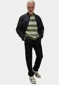 Černá bomber bunda, zelené pruhované tričko, tmavé kalhoty a béžové tenisky. Oblečení má volný střih a minimalistický design.