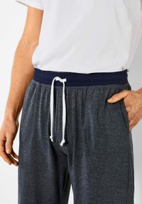Grijze joggers met een marineblauwe elastische tailleband, witte trekkoord en zijzakken. Het materiaal heeft een zachte textuur met een subtiel gemêleerd patroon.