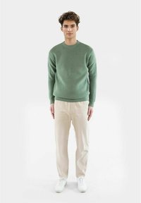 Mintgrønn ribbestrikket genser med rund hals, brukt sammen med kremfarget, teksturert bukser og hvite joggesko. Modellen står mot en ensfarget bakgrunn.