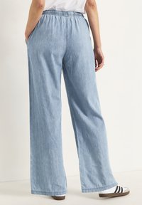 Ljusblå, vida byxor med elastisk midja, sidofickor och en slät denimstruktur, kombinerat med svart-och-vita randiga skor.