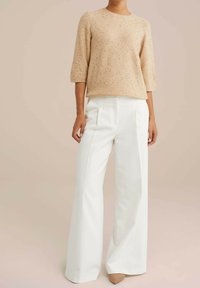Beige strukturerad stickad tröja med trekvartsärmar, kombinerad med högmidjade vita vida byxor och nakna spetsiga klackar.