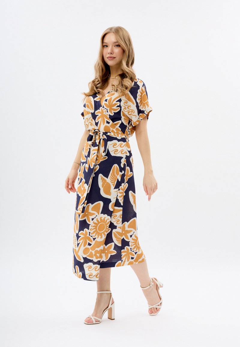 Robe marine à imprimé floral avec manches courtes, taille cintrée et jupe fluide. Agrémentée de fleurs orange et de tourbillons. Associée à des talons à lanières.