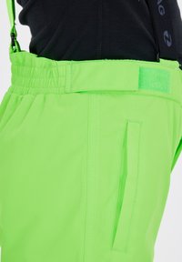 Pantaloni da neve neon verdi con spalline regolabili, vita elastica, tasca laterale e superficie liscia, progettati per attività invernali.