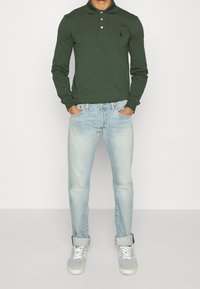 Tmavě zelená polokošile s dlouhým rukávem a třemi knoflíky, spárovaná se světle modrými zkrácenými džíny a šedými teniskami s bílými tkaničkami.