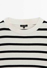 Gros plan sur un pull côtelé de couleur crème avec des rayures horizontales noires et un col rond.