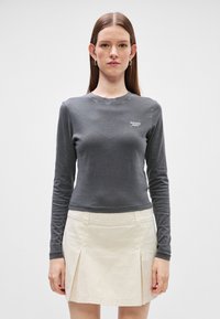 Γκρι μακρυμάνικη μπλούζα με στρογγυλή λαιμόκοψη, που διαθέτει ένα μικρό λευκό λογότυπο "tommy jeans"· συνδυασμένη με μια ανοιχτό μπεζ πλισέ φούστα.