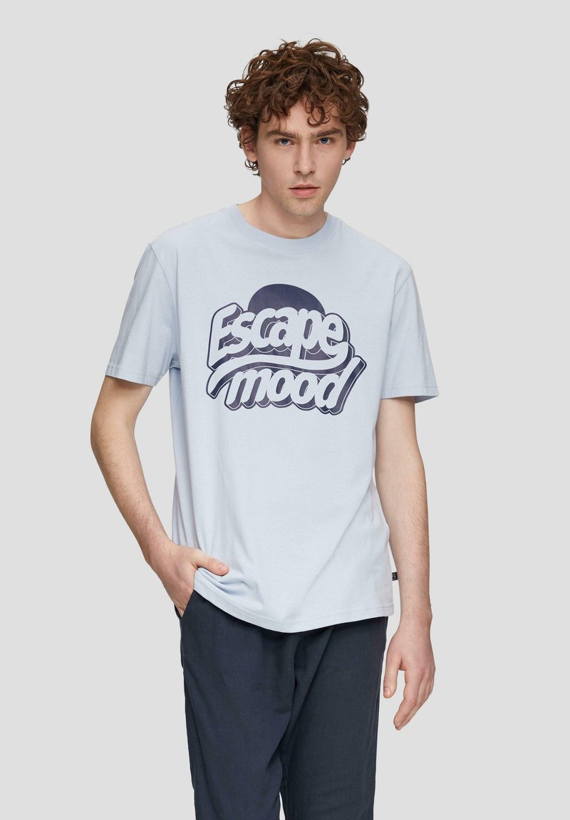 Světle modré bavlněné tričko s kulatým výstřihem, na kterém je velká tmavě modrá grafika "Escape mood". Krátké rukávy a uvolněný střih.
