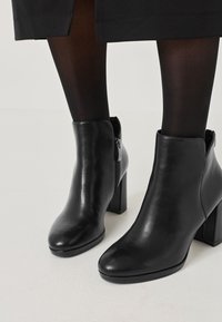 Zwarte leren enkellaarzen met een vierkante hak, afgeronde neus, ritssluiting aan de zijkant en een gladde textuur tegen een lichte achtergrond.