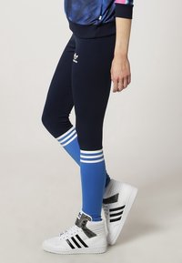 Námořnické legíny s modrými manžetami, tři bílé pruhy na kotníku. Spárovány s bílými vysokými teniskami s černými akcenty a logy.